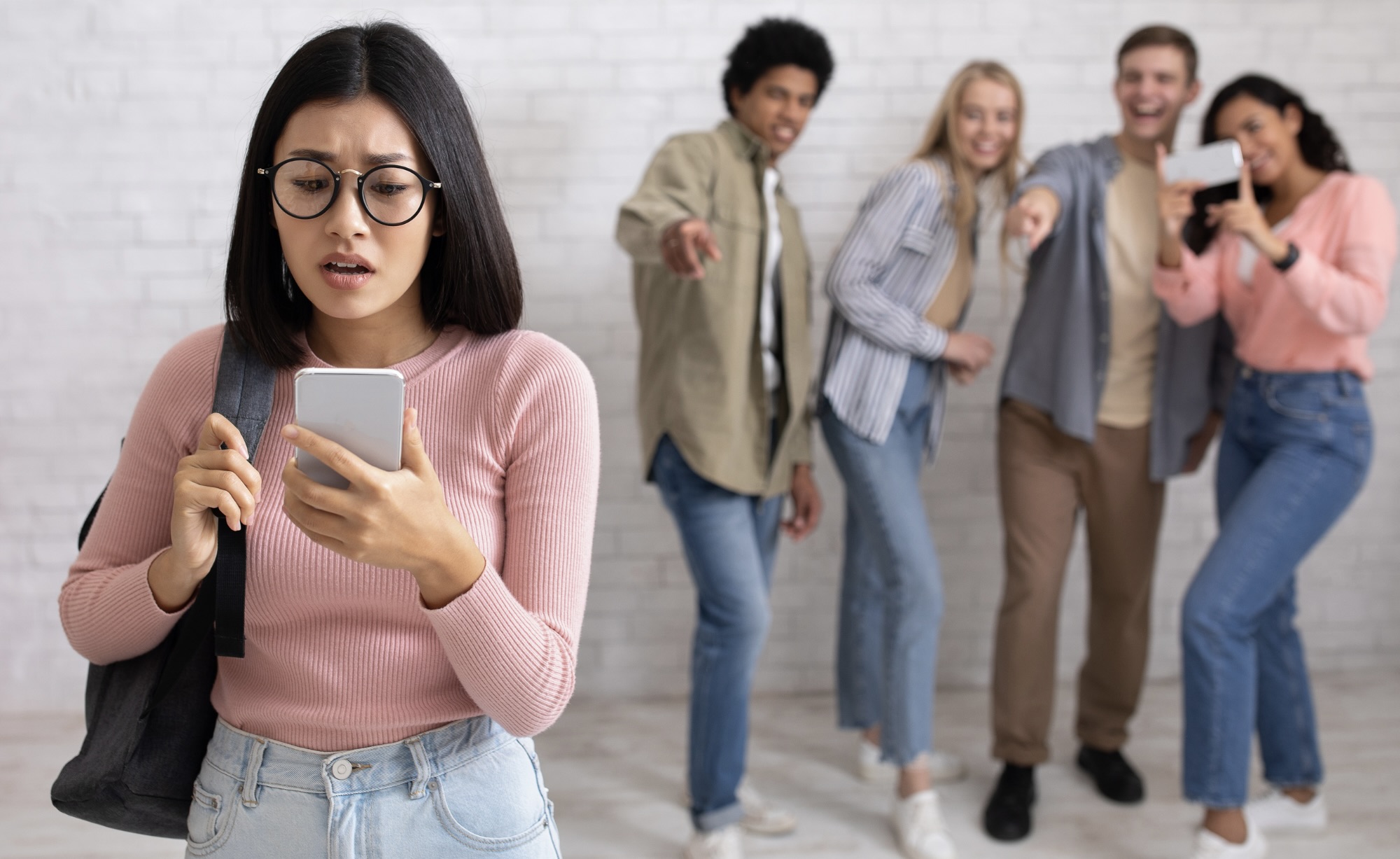 Groep jongeren lacht meisje uit die naar haar telefoon fronst