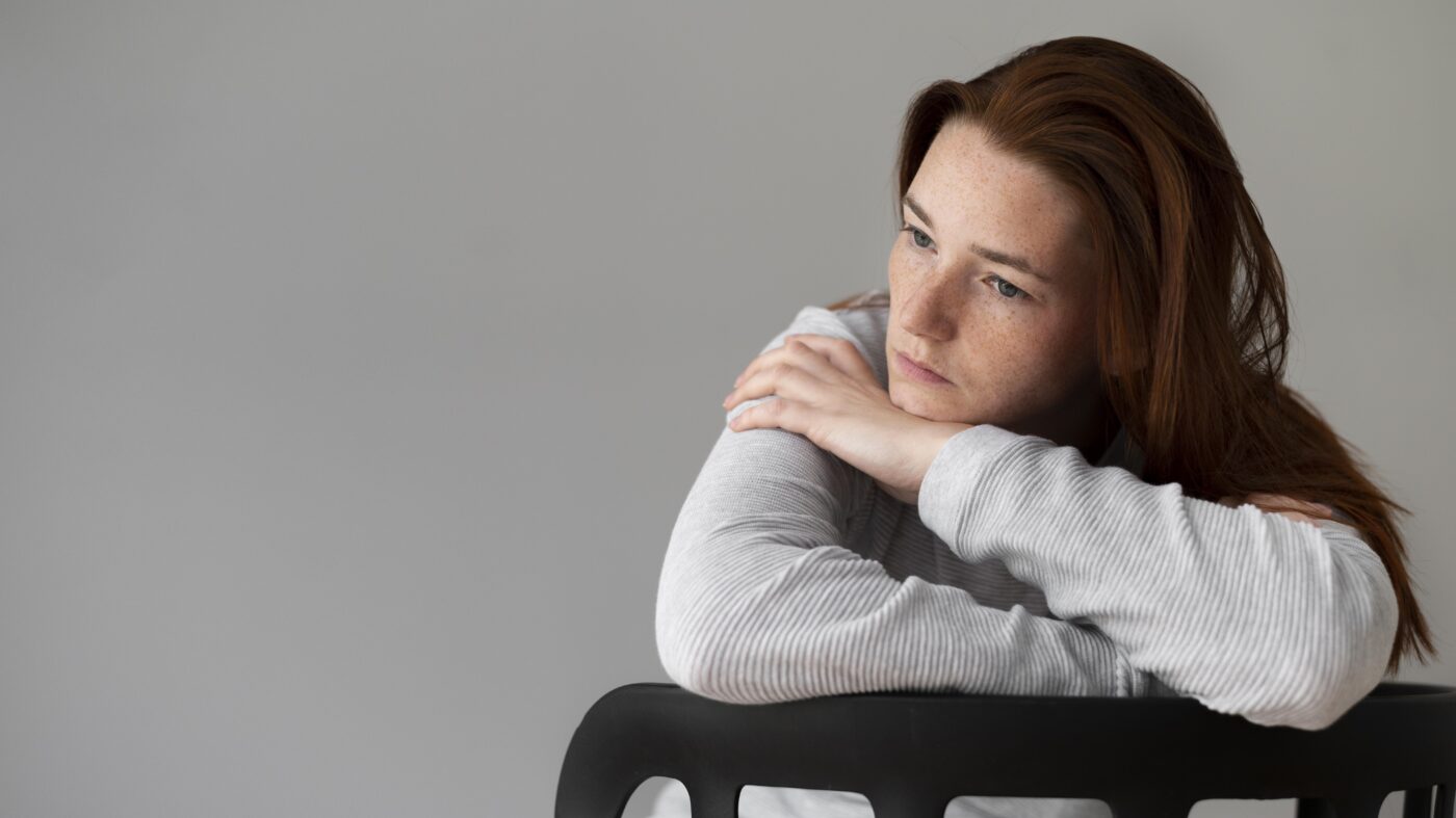 Een jonge vrouw met een vermoeide en sombere uitdrukking, leunend op een stoel, als symbool voor de dinsdagdip die jongeren ervaren na een weekend van feesten en middelengebruik.