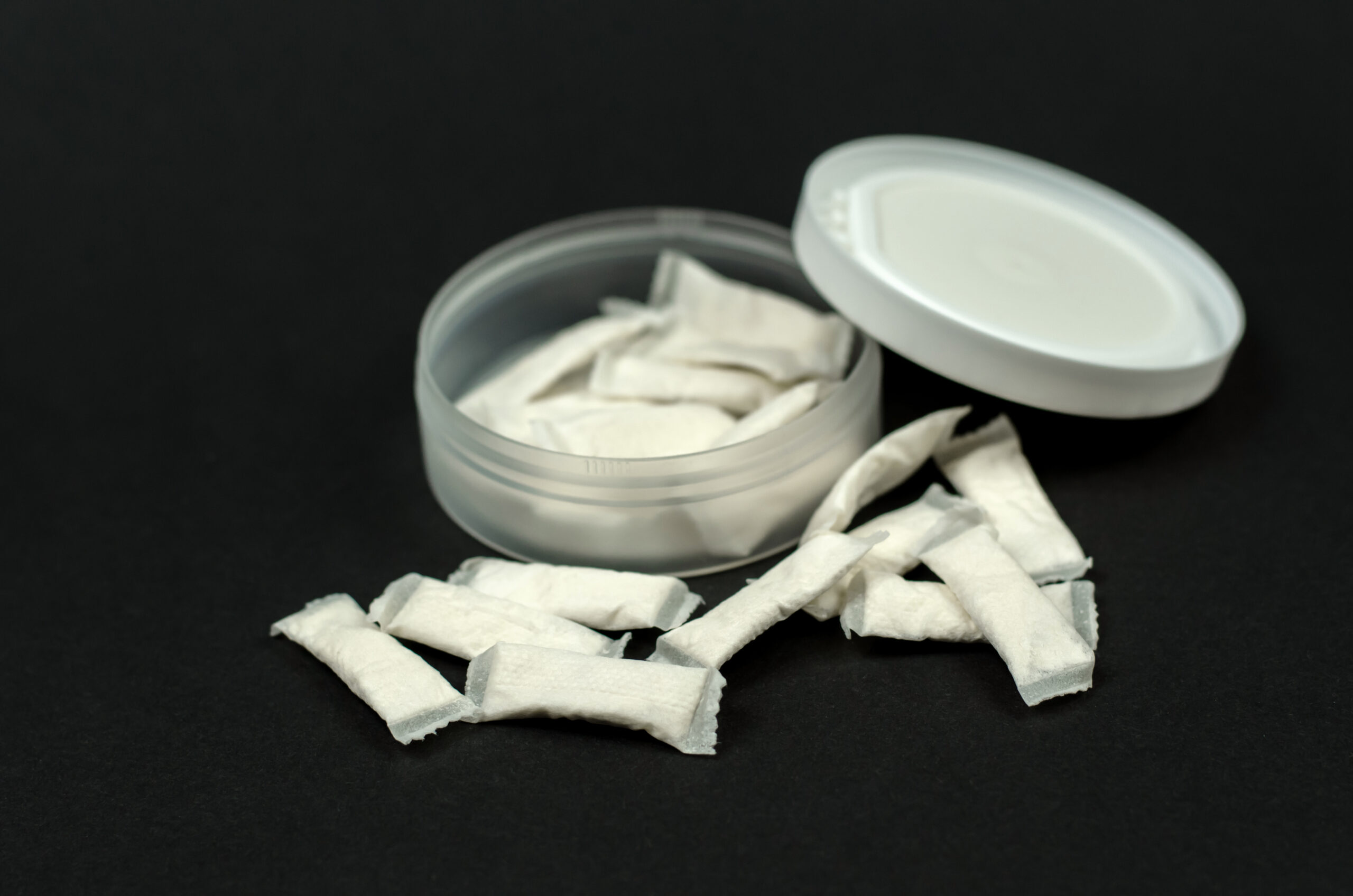 Witte nicotinezakjes (snus) in open rond plastic doosje op zwarte achtergrond
