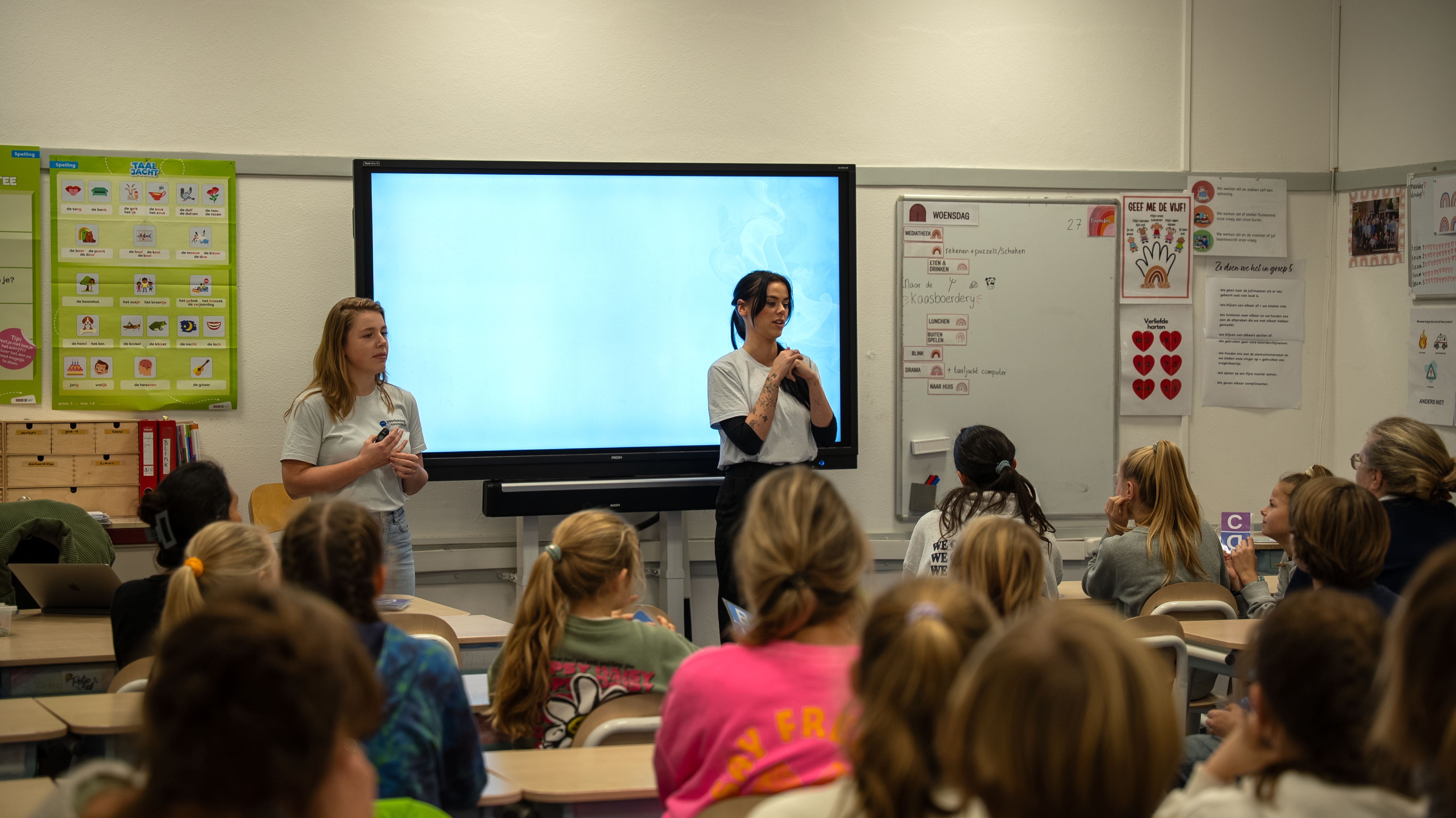 Twee voorlichters spreken in de klas over racisme en discriminatie, met leerlingen die aandachtig luisteren en actief meedoen aan het gesprek.