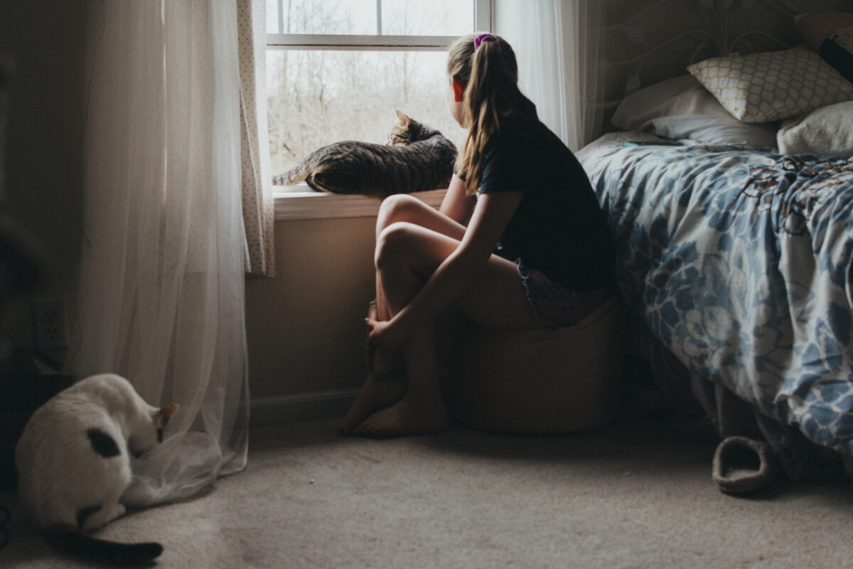 Meisje kijkt bezorgd uit het raam met kat naast zich, symbool voor angst door TikTok-hoax National Rape Day