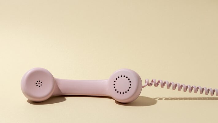 Lichtroze vintage telefoonhoorn op een beige achtergrond, als metafoor voor belangst bij jeugd