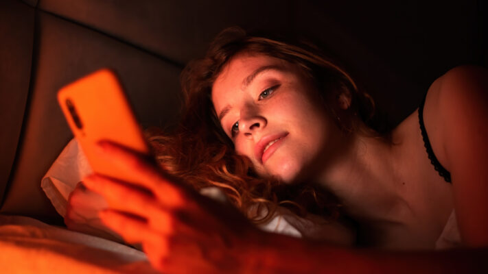 Tienermeisje ligt in bed en kijkt op haar smartphone, belicht door rood schermlicht