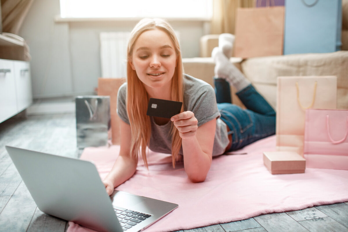 Jong meisje ligt op de grond met een laptop en creditcard.