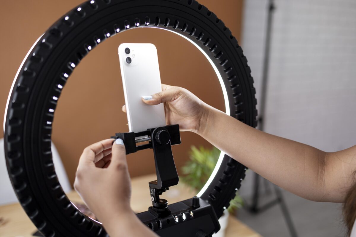 Een jonge vrouw plaatst haar smartphone in een ringlamp – het symbool van moderne online zichtbaarheid via TikTok en livestreams.