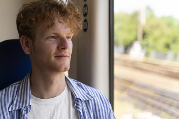 Jongere in de trein kijkt rustig uit het raam tijdens een raw dogging-moment zonder scherm of oordopjes