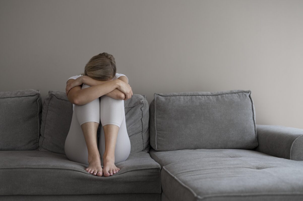 Jonge vrouw met mentale klachten zit verdrietig op de bank met haar hoofd in haar armen