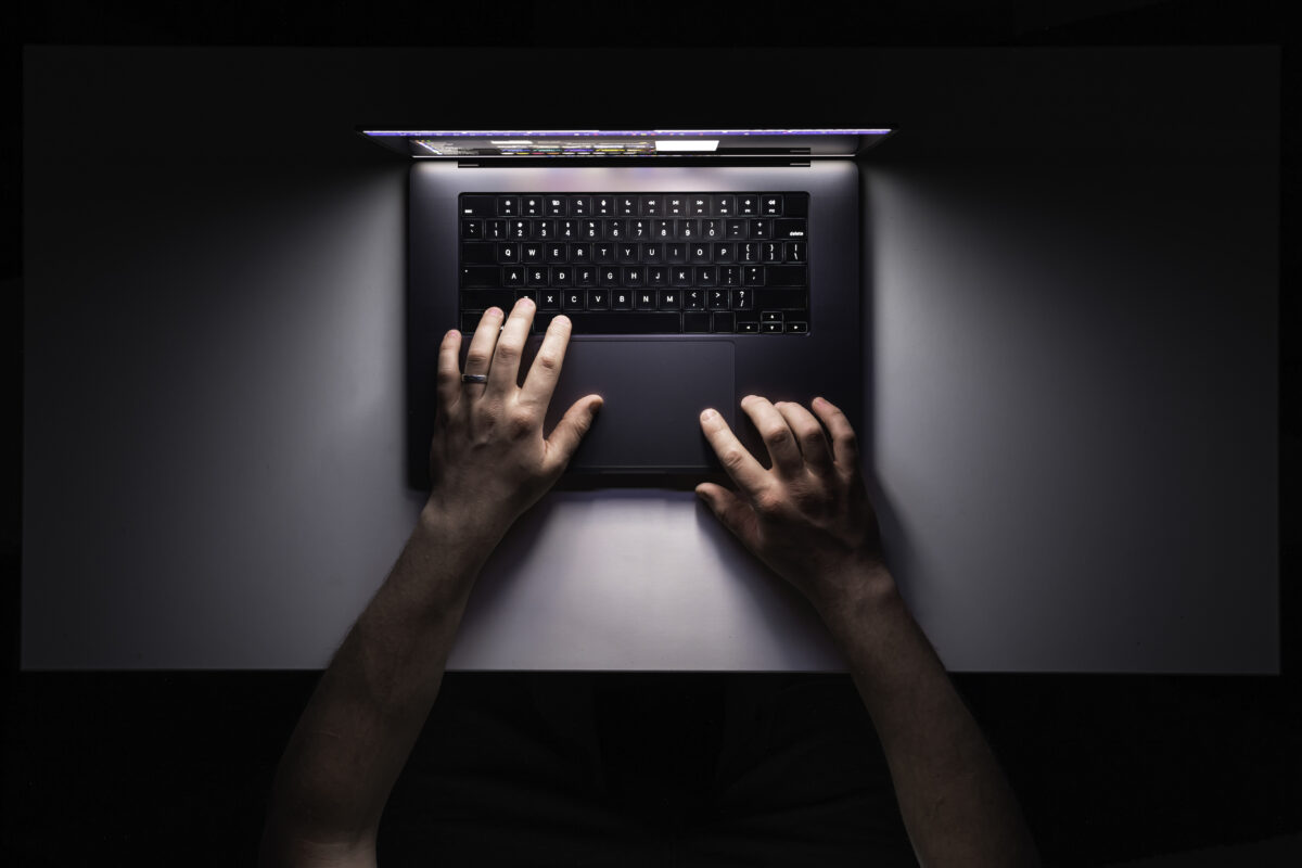 Handen van een persoon die 's avonds achter een laptop zit, symbool voor cyberpesten.