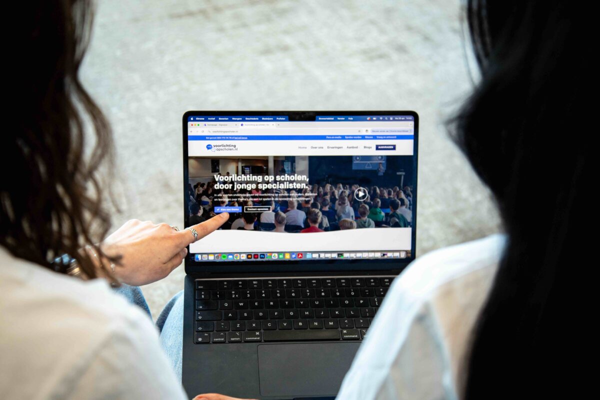 Twee mensen bekijken de website van Voorlichting op Scholen op een laptop.
