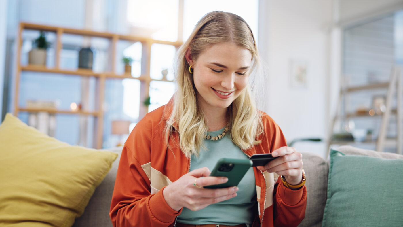 Jonge vrouw doet een online aankoop met telefoon en betaalpas, symbool voor het gemak én risico van achteraf betalen door jongeren.