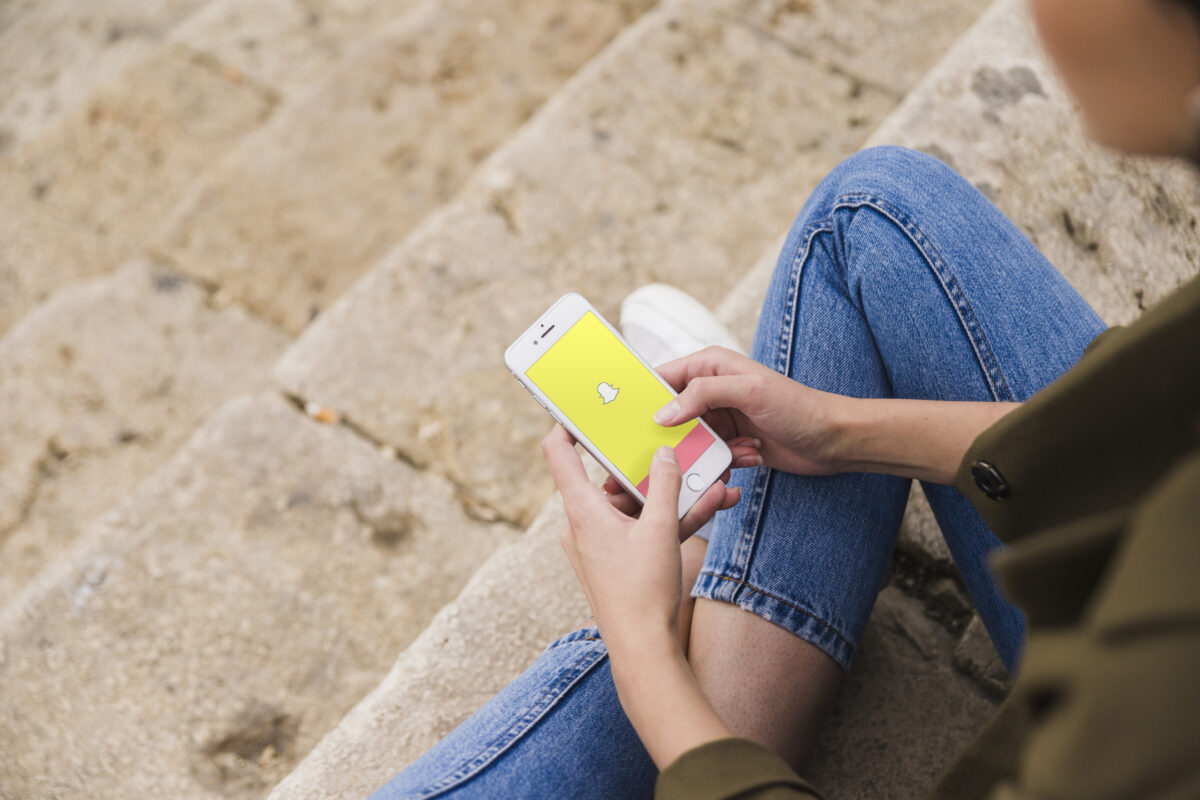 Jongere zit op een trap en opent Snapchat op haar smartphone, symbool voor online ronselpraktijken via sociale media.