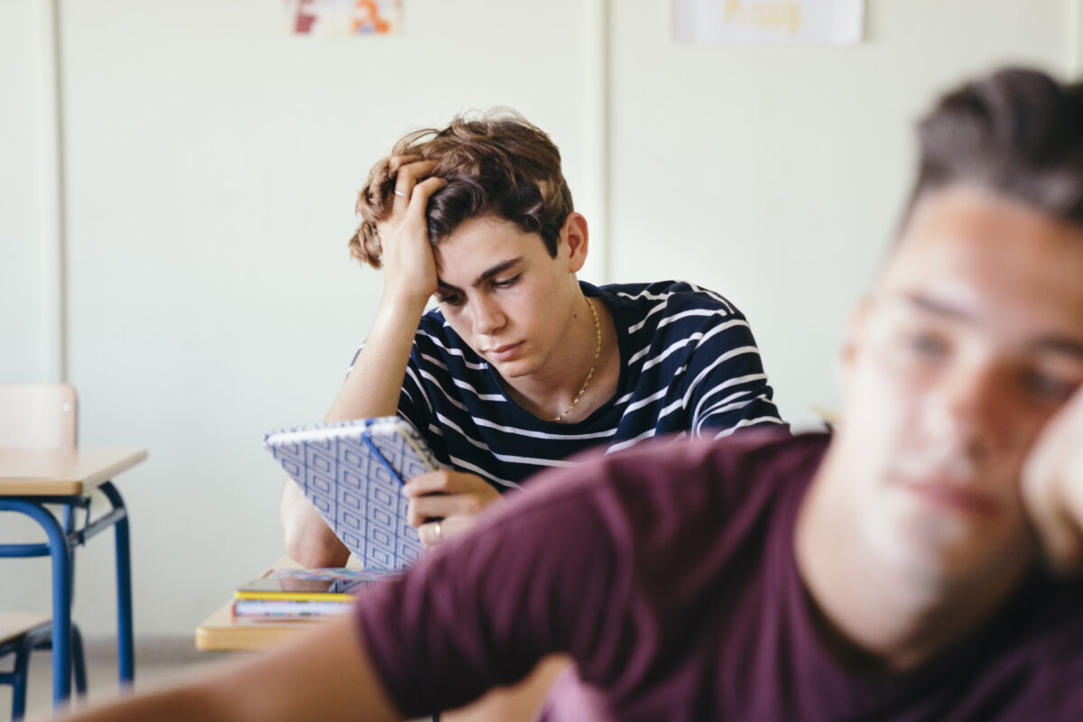 Tiener met vermoeide blik en schoolschrift in de klas.
