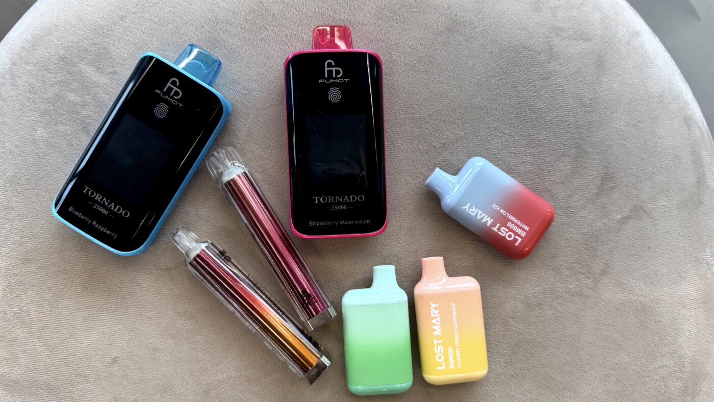 Verschillende felgekleurde vapes van merken als Tornado en Lost Mary op een tafel, symbool voor de populariteit van vapen onder jongeren.