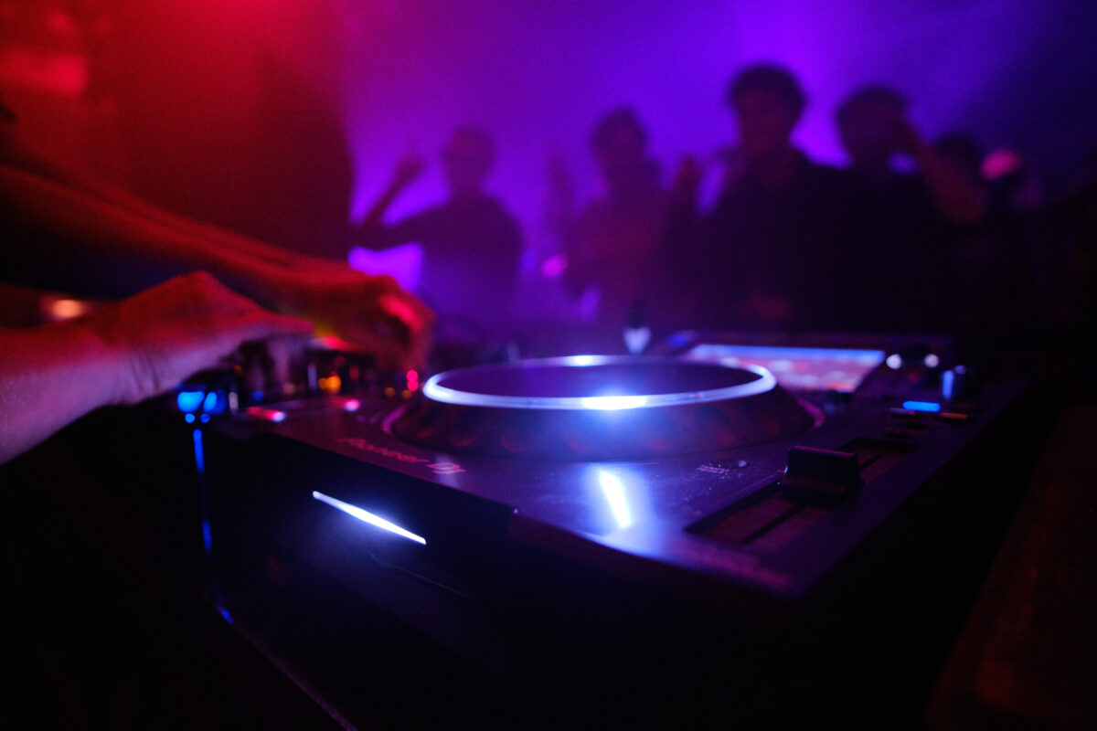 DJ draait muziek in een club waar jongeren dansen tijdens het uitgaan.