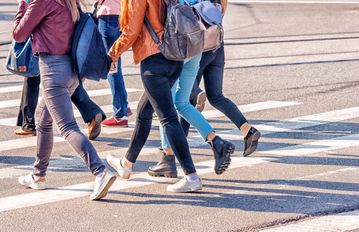 Groep jongeren met rugzakken steekt samen een zebrapad over onderweg naar school.