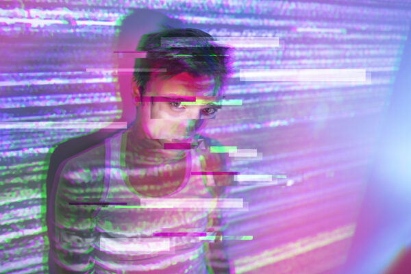 Jongere kijkt in felgekleurde digitale lichtprojectie met glitch-effect, symbool voor verdwalen in online prikkels en goonen.