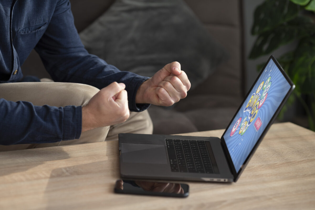 Persoon balt zijn vuisten van blijdschap terwijl hij achter een laptop zit met een spel op het scherm.