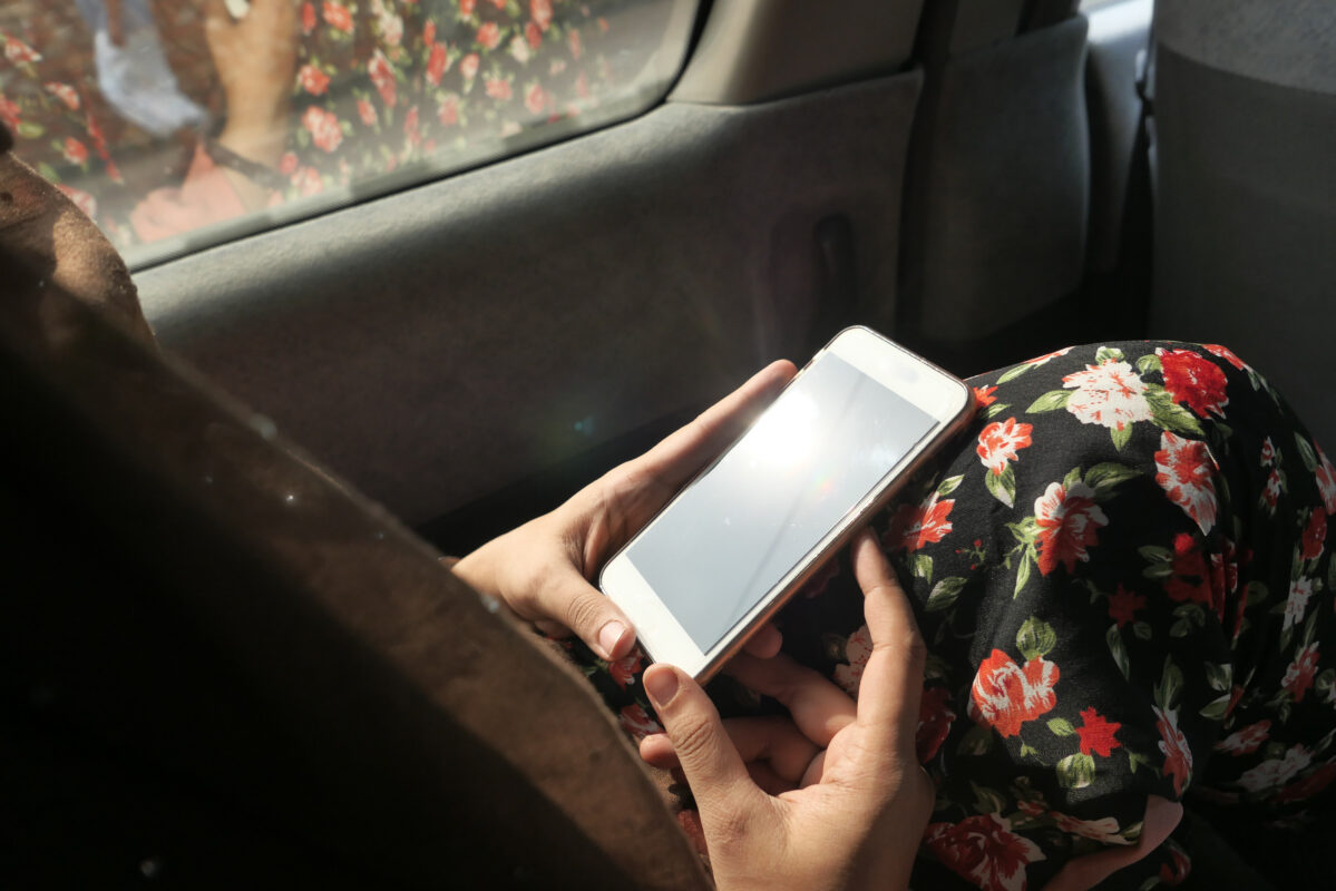 Persoon houdt een smartphone vast terwijl die in een auto zit, met zonlicht dat op het scherm weerkaatst.
