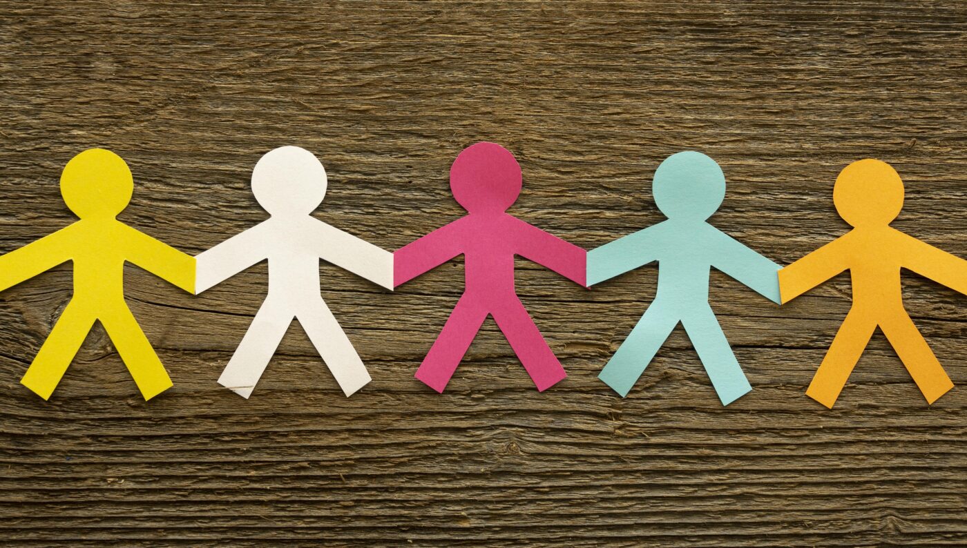 Gekleurde papieren figuren die hand in hand staan, als symbool voor verbondenheid en burgerschap.
