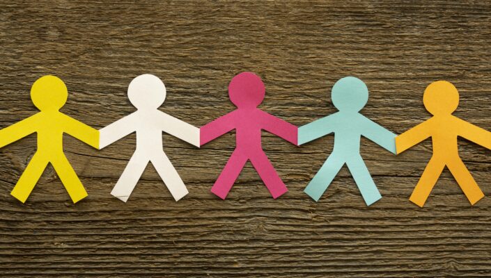 Gekleurde papieren figuren die hand in hand staan, als symbool voor verbondenheid en burgerschap.