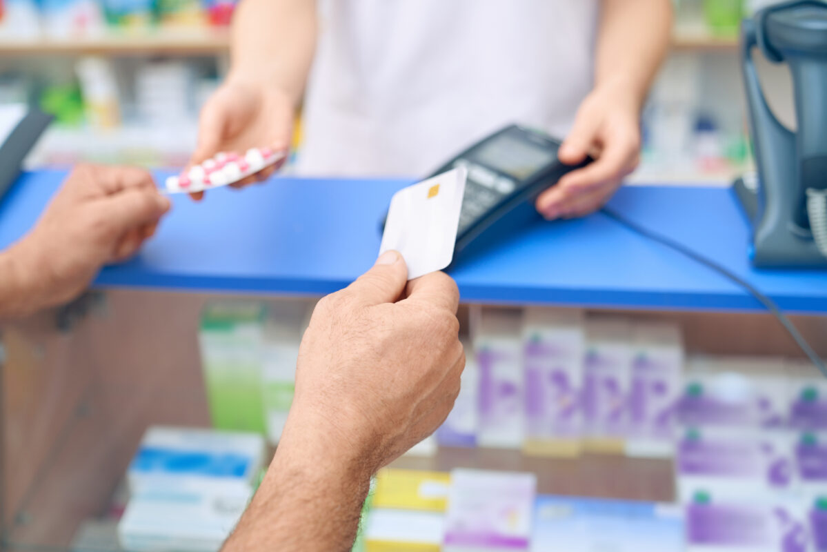 Persoon betaalt bij een apotheek met een pinpas terwijl medicijnen worden aangereikt door een medewerker.
