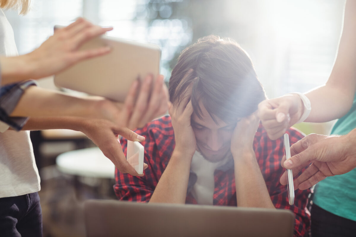 Jongere met het hoofd in de handen terwijl meerdere mensen om hem heen om aandacht vragen, symbool voor stress en overbelasting.