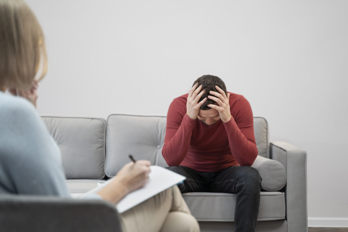 Man zit met gebogen hoofd en handen tegen zijn hoofd tijdens gesprek met psycholoog over psychische klachten en mentale gezondheid.