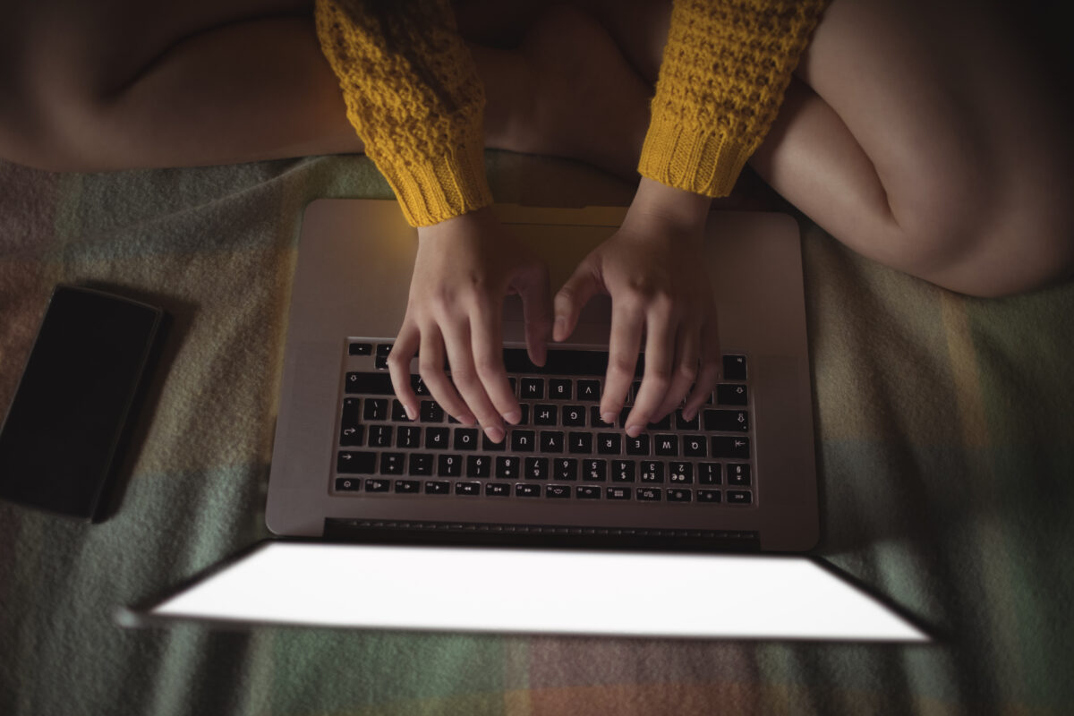 Jongere zit op bed en gebruikt een laptop en smartphone, symbool voor online risico’s en online seksueel misbruik
