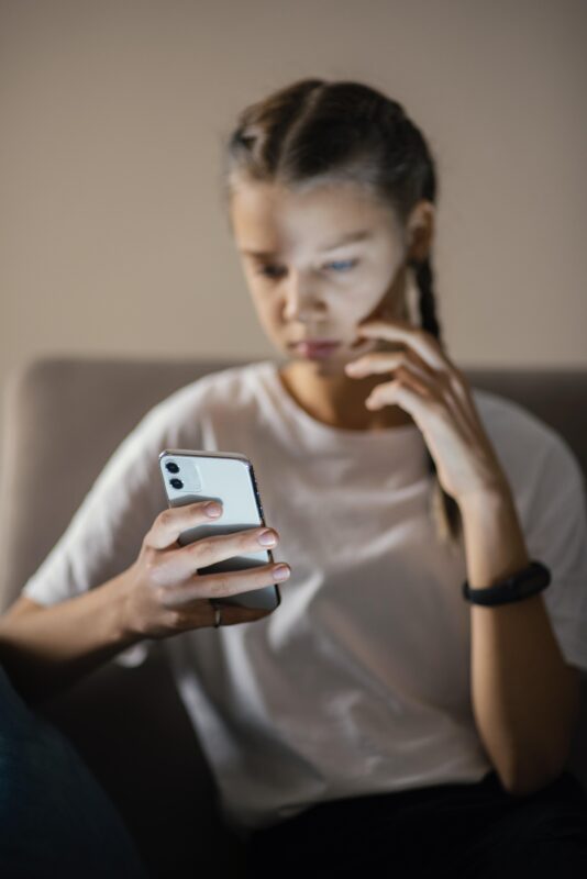Jong meisje kijkt gespannen naar haar smartphone terwijl ze online berichten leest op de bank.