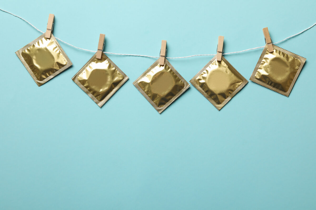 Gouden condoomverpakkingen hangen aan een waslijn tegen blauwe achtergrond als symbool voor condoomgebruik onder jongeren