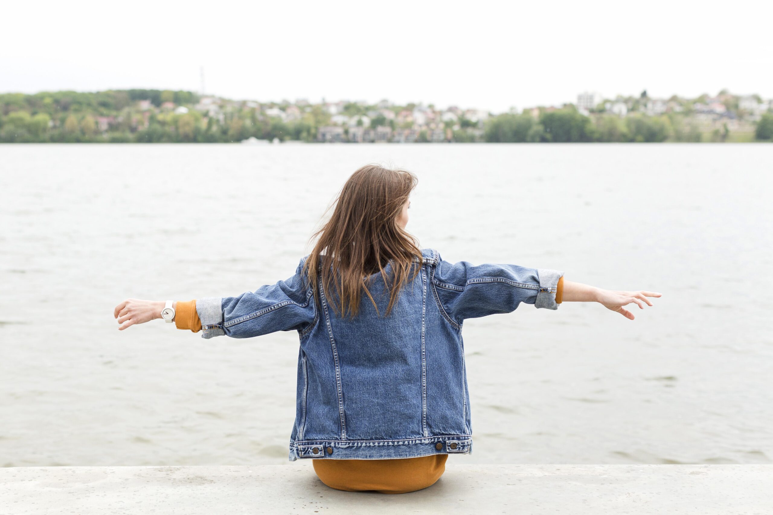 Jongere zit met gespreide armen aan het water en kijkt uit over een rustige omgeving.