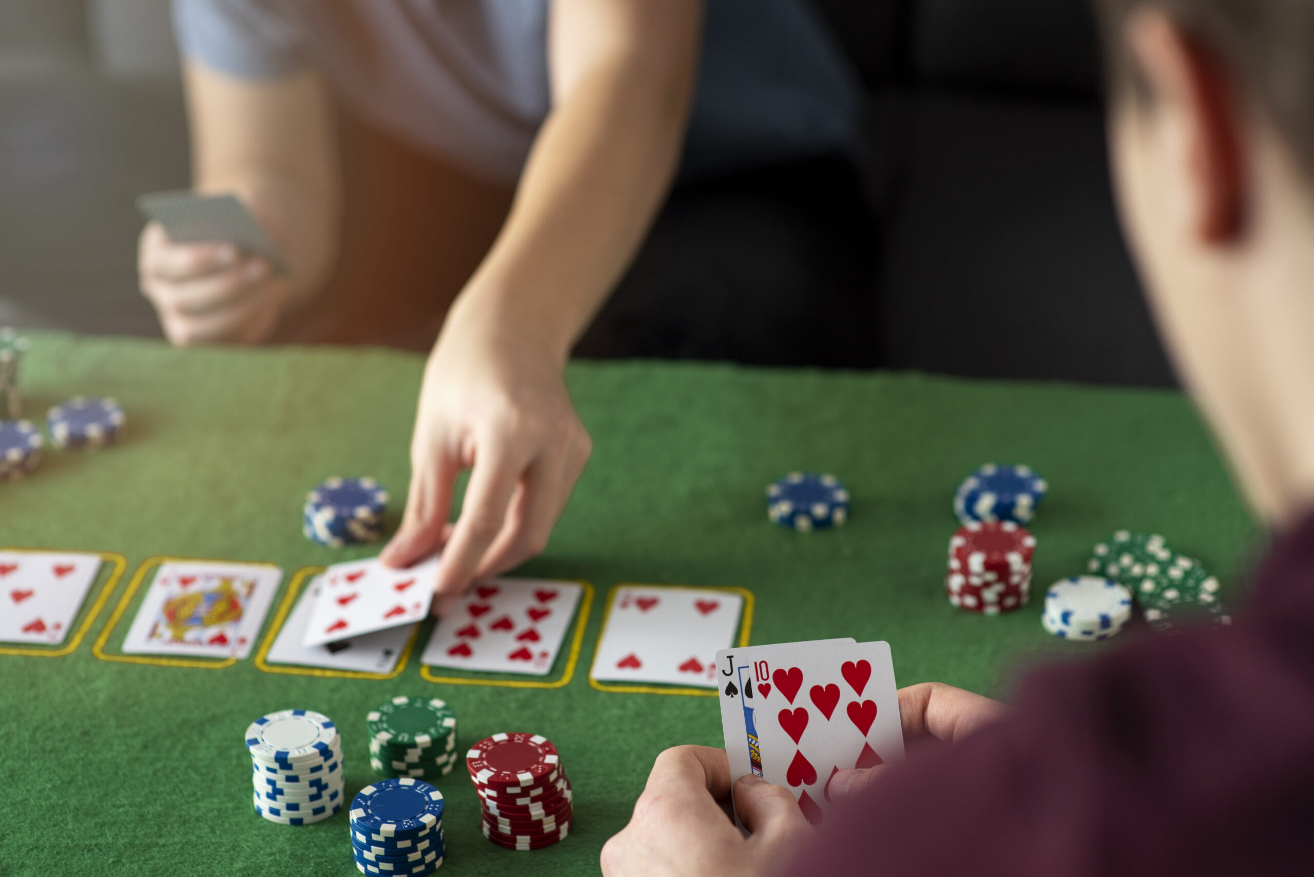 Jongeren spelen poker aan tafel met speelkaarten en fiches, focus op kaarten en stapels chips.