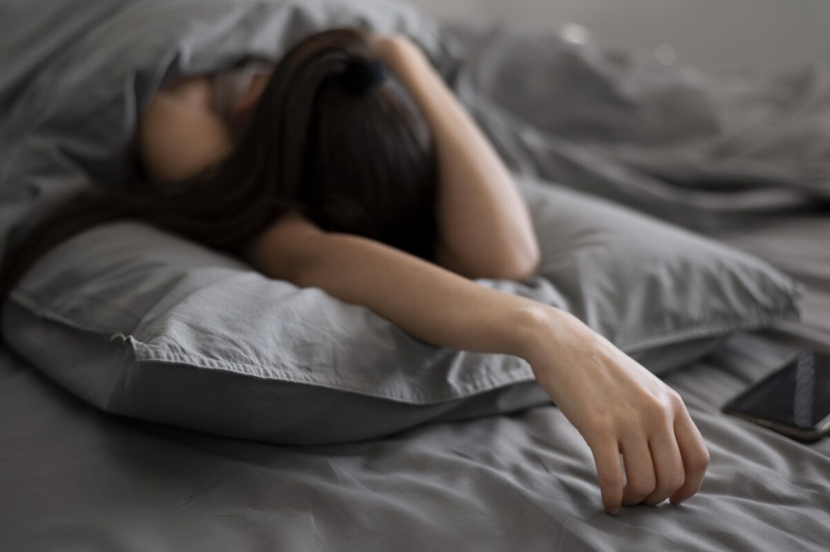 Jongere ligt uitgeput in bed met telefoon naast zich, symbool voor slapeloosheid en het zoeken naar rust via online middelen.