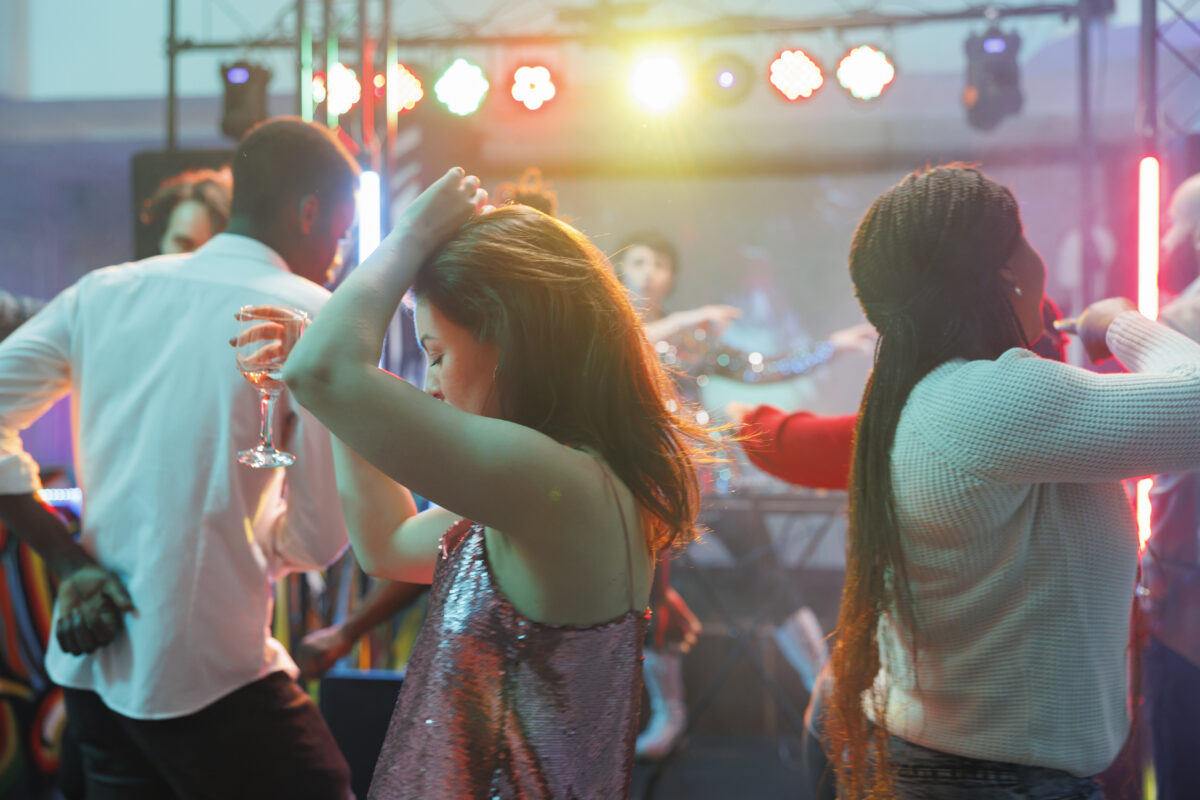 Jongeren dansen in een club met gekleurde lichten terwijl een meisje een drankje vasthoudt.