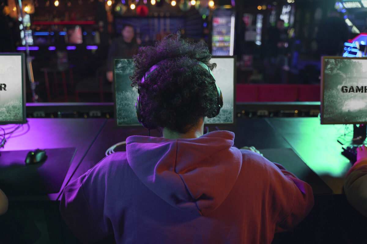 Jongere met koptelefoon zit achter een computer en gamet in een donkere ruimte met kleurrijke verlichting