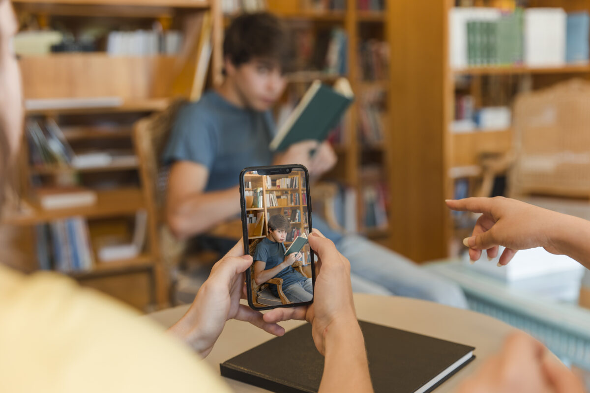 Jongere wordt gefilmd door klasgenoten terwijl hij een boek leest in een bibliotheekomgeving