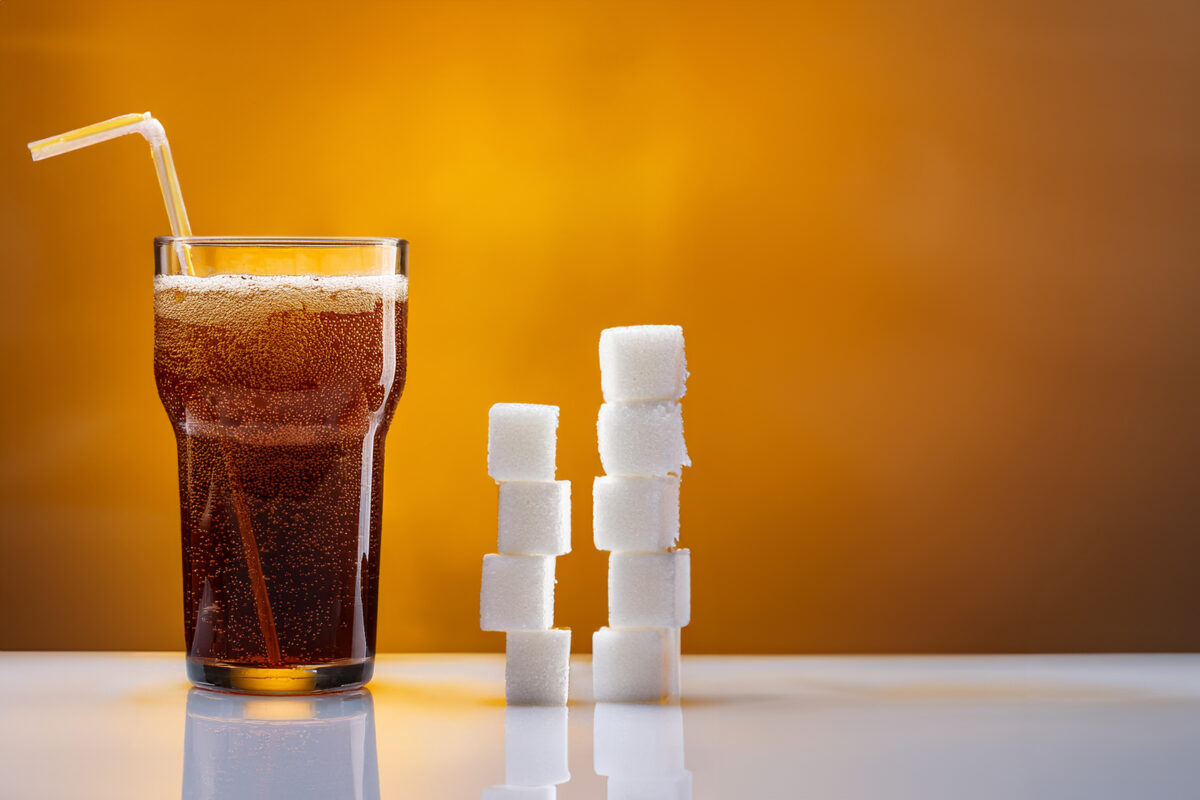 Glas frisdrank met daarnaast gestapelde suikerklontjes die de hoeveelheid suiker in frisdrank visualiseren