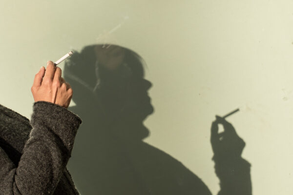 Jongere houdt een sigaret vast terwijl haar schaduw zichtbaar is op de muur