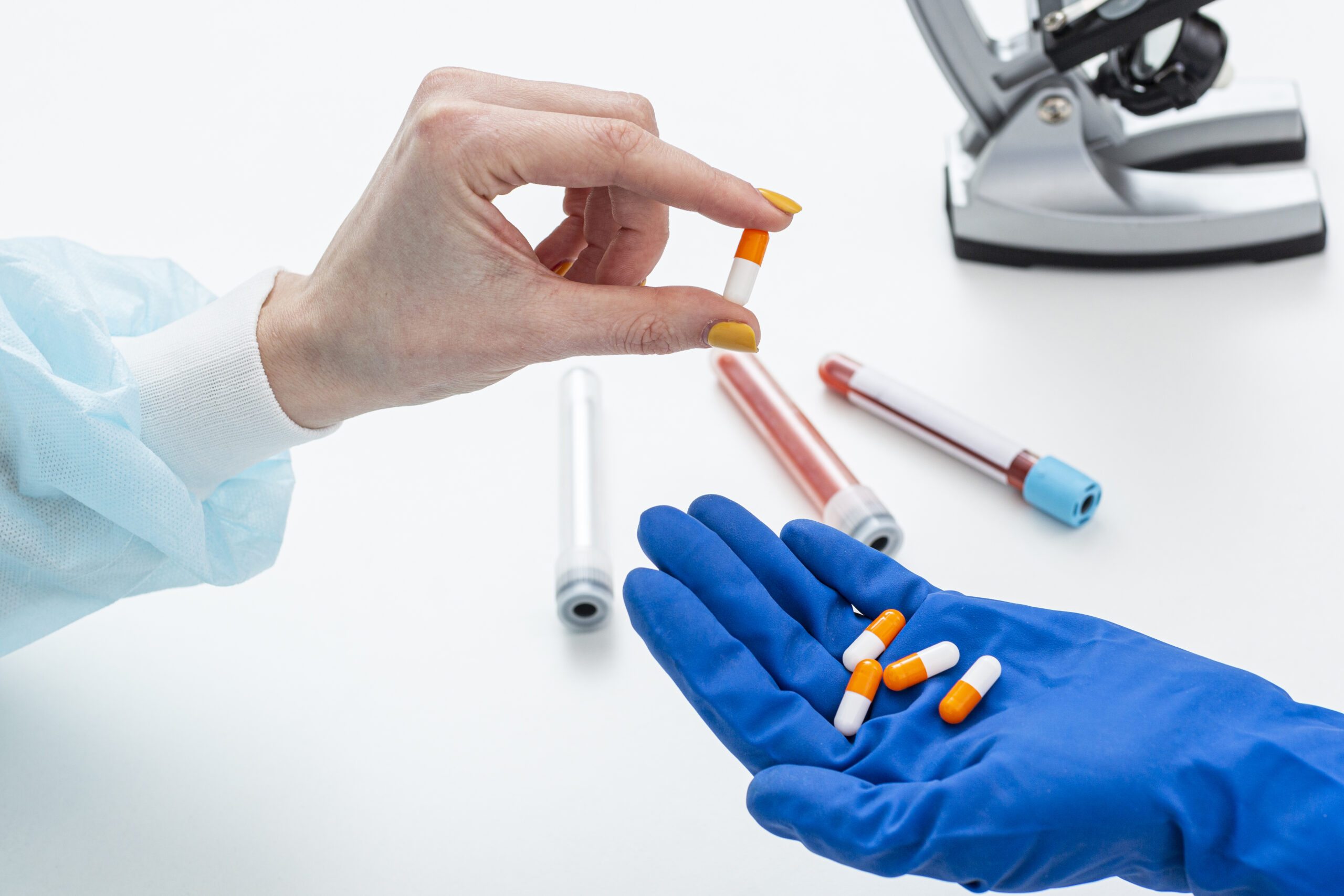 Handen met handschoenen houden capsules vast terwijl een andere hand een pil aanreikt voor onderzoek
