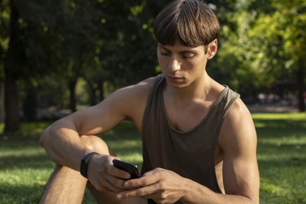 Jongen kijkt op zijn telefoon tijdens een workout in het park, mogelijk beïnvloed door online content over gezondheid en testosteron