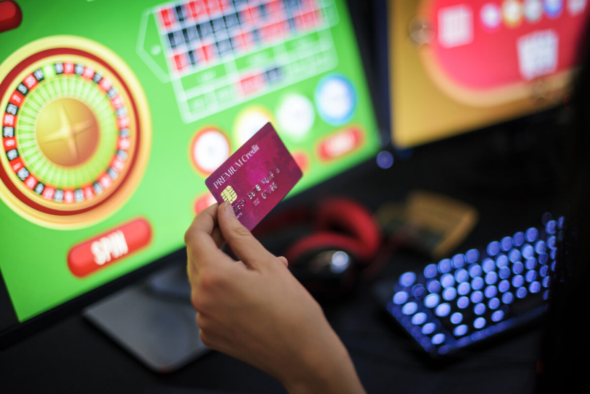 Jongere houdt creditcard vast terwijl online roulette wordt gespeeld op een computer