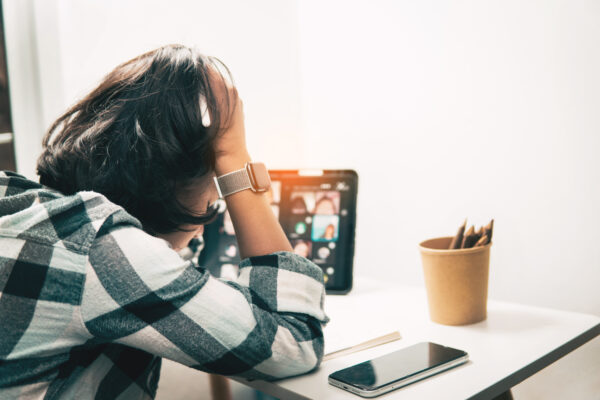 Jongere zit met hoofd in handen achter een tablet en smartphone, zichtbaar gestrest tijdens online activiteit