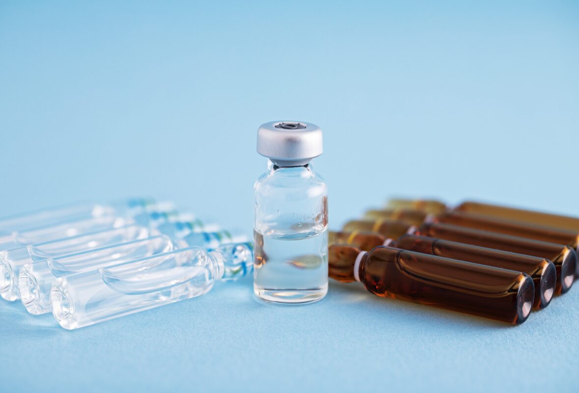 Glazen flacon met vloeistof en meerdere ampullen met injectievloeistoffen op een blauwe achtergrond