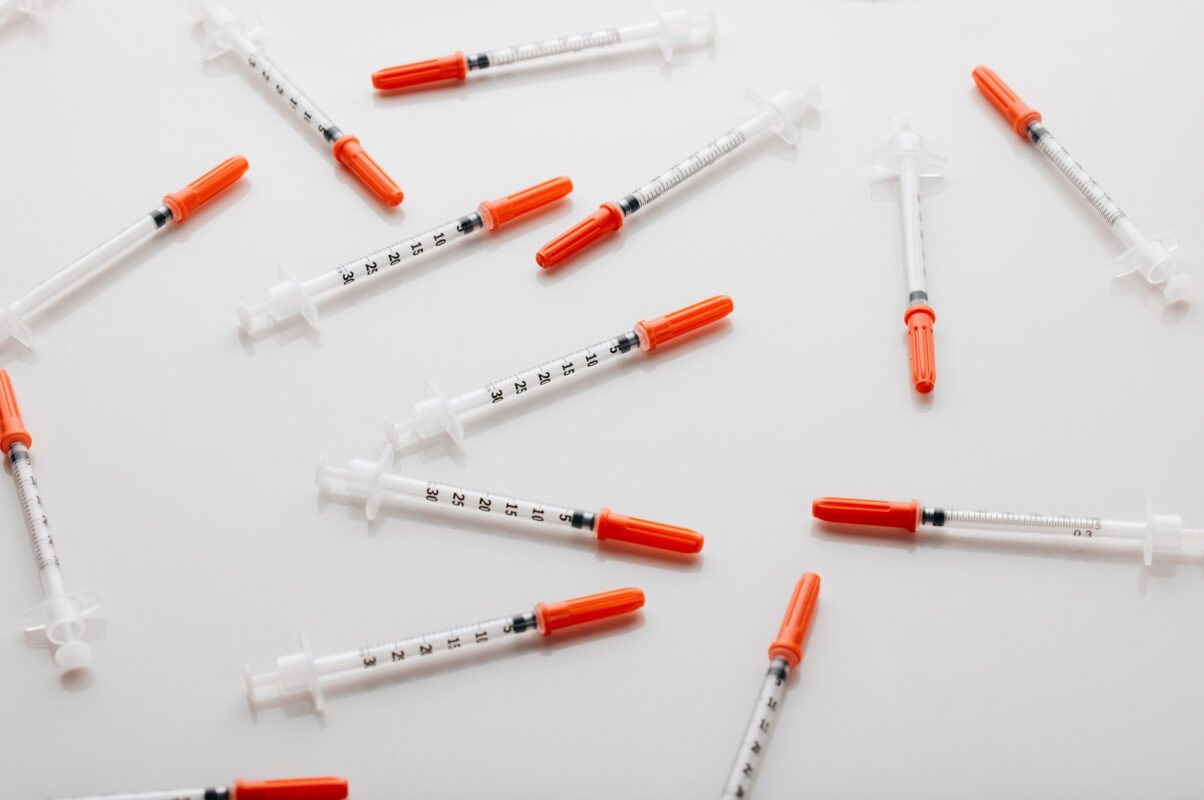 Injectiespuiten verspreid op een witte achtergrond, passend bij een artikel over peptides en online fitnesstrends onder jongeren.