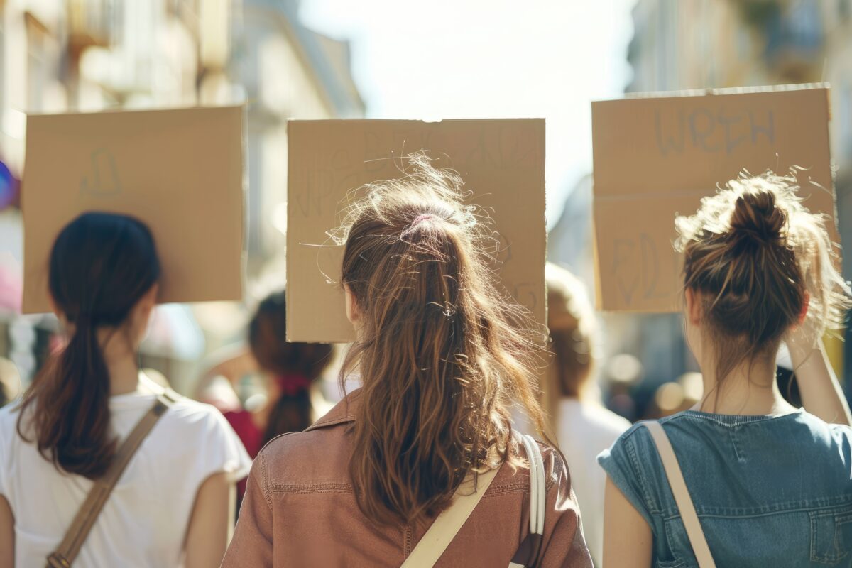 Drie jonge vrouwen lopen met protestborden door een drukke straat tijdens een demonstratie, passend bij discussies over online vrouwenculturen, identiteit en de opkomst van de femosphere.
