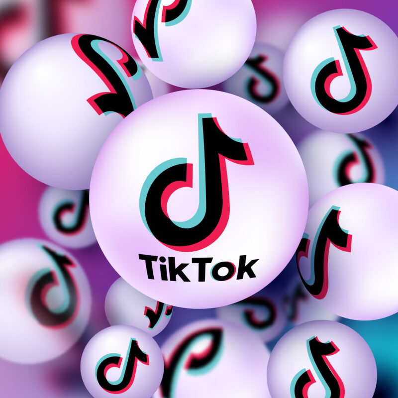 Illustratie van meerdere zwevende TikTok-logo's op witte bollen tegen een roze, paarse en blauwe achtergrond. De afbeelding symboliseert TikTok en de groeiende invloed van het platform op jongeren en online koopgedrag.