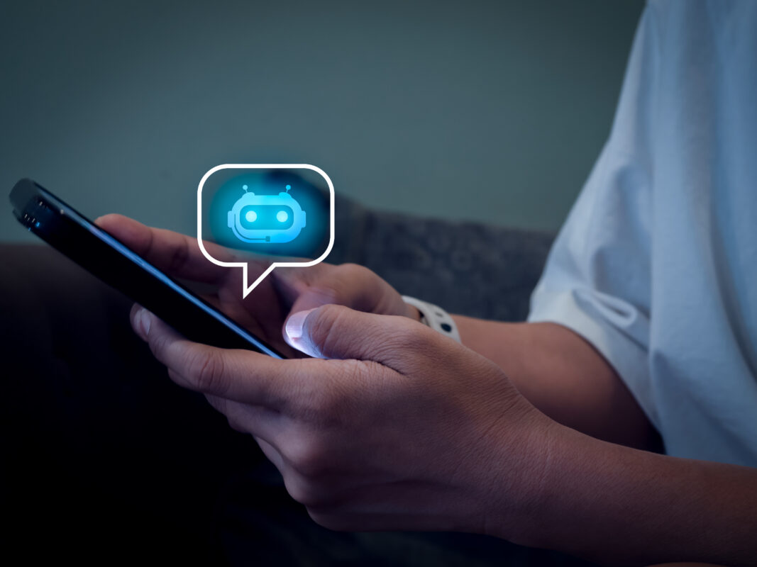 Jongere gebruikt een smartphone terwijl een digitaal chatbot-icoon in een tekstballon boven het scherm verschijnt, als illustratie van AI-chatbots en online gesprekken.