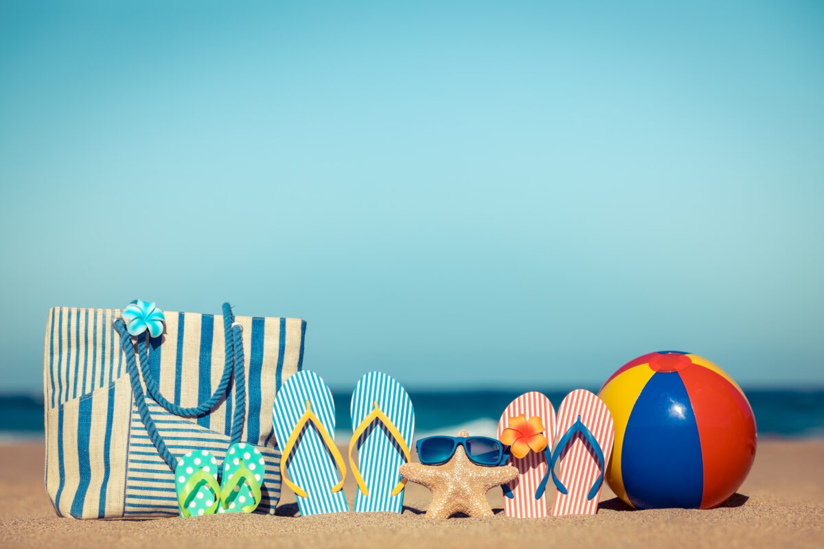 Strandtas, slippers, zonnebril en strandbal op het strand als symbool voor de zomervakantie en meer vrije tijd online.