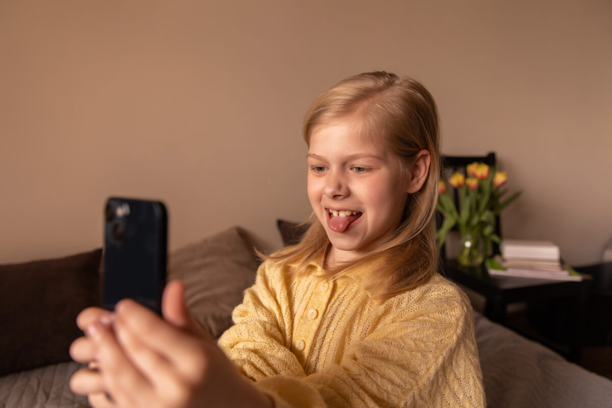 Jong meisje maakt thuis een selfie met haar smartphone. De afbeelding illustreert hoe ook jonge kinderen actief zijn op sociale media zoals Snapchat.