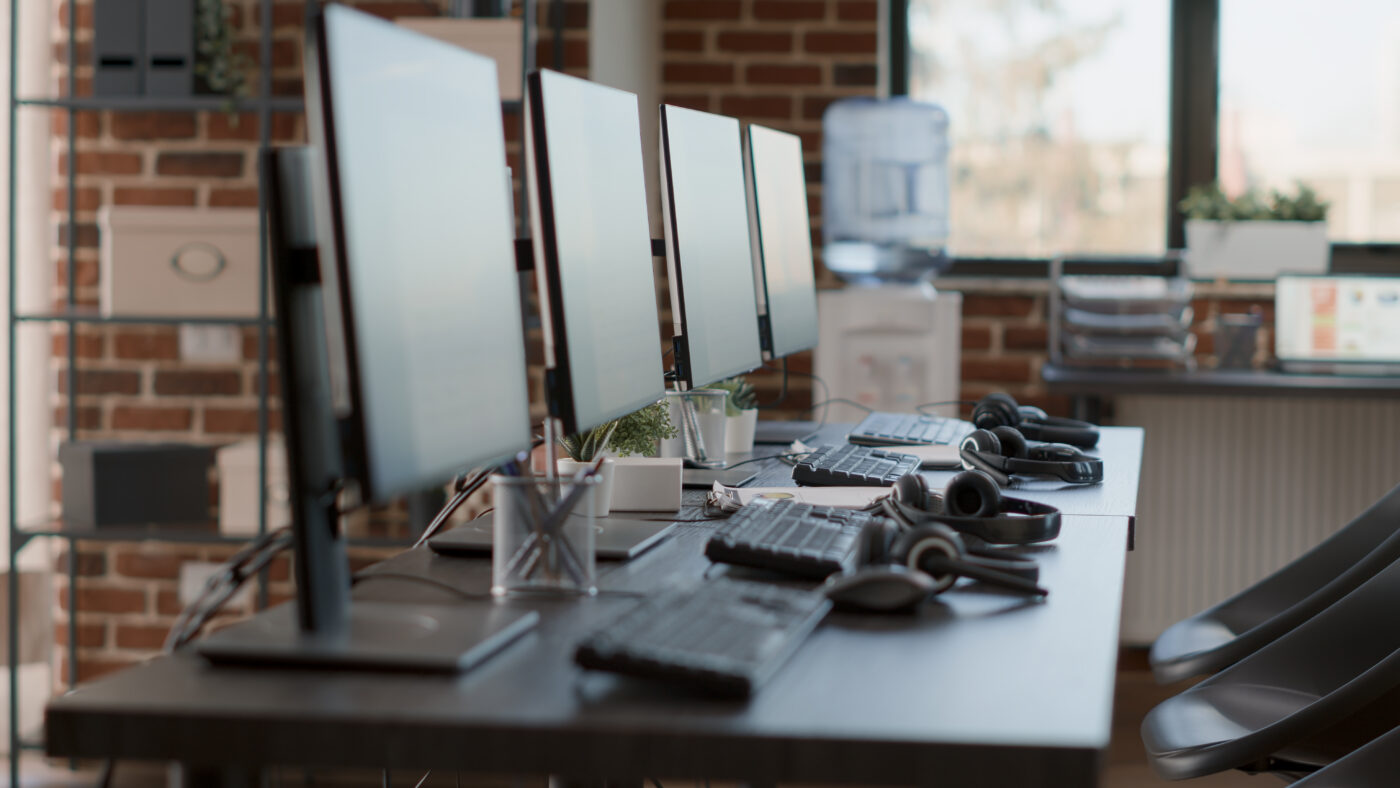 Werkplekken met computers, toetsenborden en headsets in een kantooromgeving. De afbeelding symboliseert een hulpchat of hulplijn waar jongeren, ouders en professionals terechtkunnen voor ondersteuning.